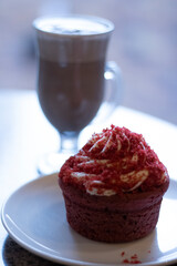 Small red cupcake in front of a glass cup with hot chocolate on a wooden table on a cold day
