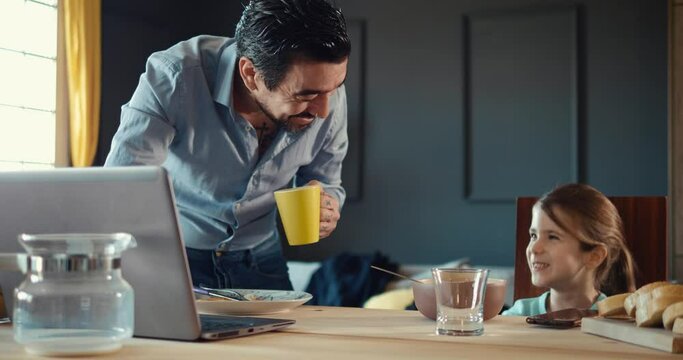 Business Dad and daughter talk over breakfast. Morning family routine before work and school. Happy tattooed man drinks coffee and talks to a little girl while eating chocolate flakes with milk.