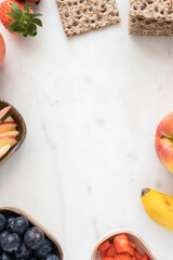 A great copy space in the middle surrounded by three trays full of fruit and a several pieces of fruit over a marble board.