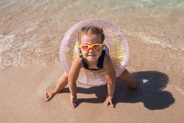 Portrait of joyful little girl with swim goggles and swimming ring having fun at the beach on summer day. Child ready to learning swimming. Wonderful family getaways. Vacation with kids concept
