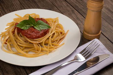 Bavette pasta with sugo sauce and basil leaves served on a plate. Fork, knife and pepper grinder. Gastronomy Photography. Tasty pasta with sauce.