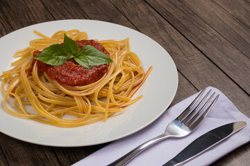 Bavette pasta with sugo sauce and basil leaves served on a plate. Fork and knife. Gastronomy Photography. Space for text.