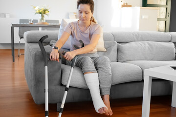 Woman in her late twenties on couch at home with elbow crutches and orthopedic plaster. Fracture of...