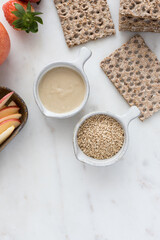 Overhead view of two bowls full of sauce and sesame seeds next to some healthy crackers over a marble board.