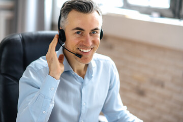 Portrait of successful, confident handsome senior businessman, manager, or call center worker, sits...