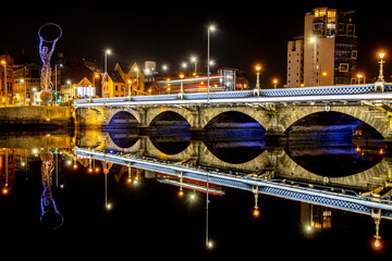 Queen's Bridge in Belfast, Northern Ireland. Long exposure of night cityscape of illuminated bridge with a bus passing through..