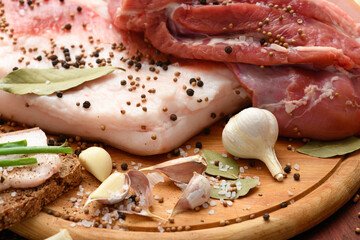 raw pork meat and lard with salt, spices and garlic on a cutting board, dark wooden background
