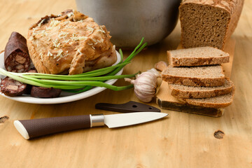 baked meat and blood sausage on a plate, green onion and garlic on wooden background, home cooking
