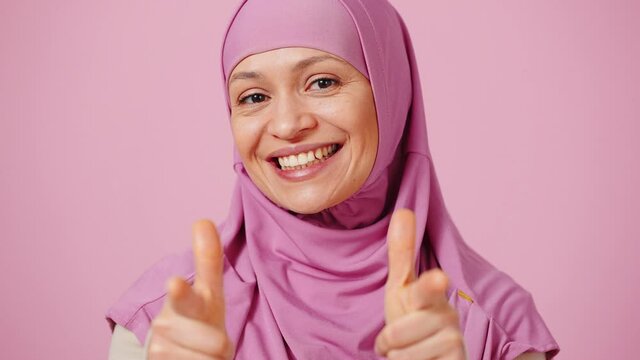 Gotcha. Close up portrait of happy middle aged islamic woman laughing and pointing to camera, pink background