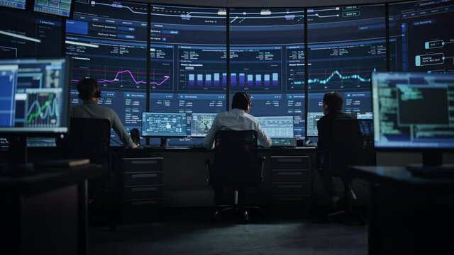 Professional IT Technical Support Specialists and Software Programmer Working on Computers in Monitoring Control Room with Digital Screens with Server Data, Blockchain Network and Surveillance Maps. 