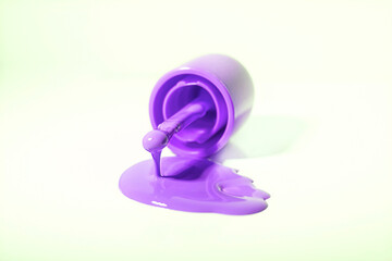 Purple colored nail polish is poured on a white table, close up, isolated