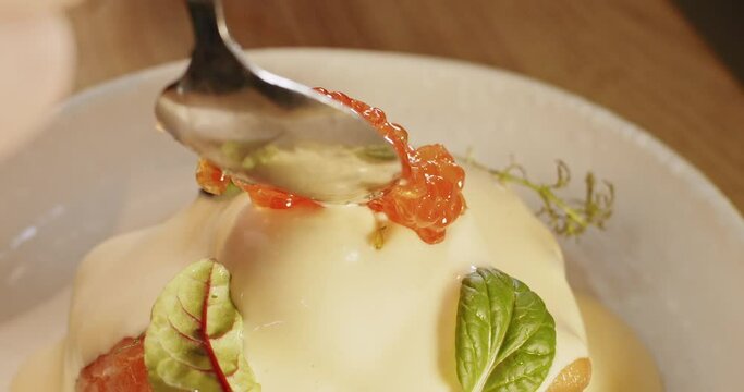 Chef decorates with a tablespoon juicy fresh red caviar benedict egg toast with parmesan hollandaise sauce and watercress salad on top in slowdown