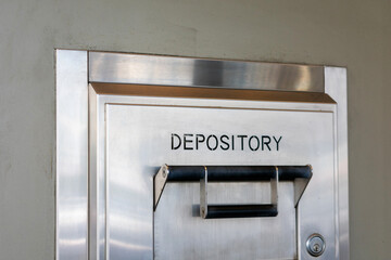 Depository sign on an exterior secured bank drop box attached to the wall of a bank building. - Powered by Adobe