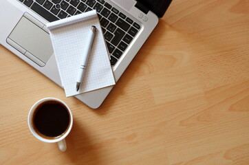 Laptop with coffee cup, notebook and pen on wooden background Top view. Concept for home office. Business concept. Work from home. Desk with laptop, blank notepad, coffee cup and pen on wooden table.