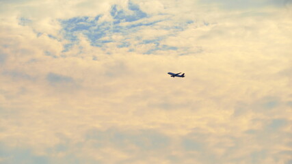 Fototapeta premium Airplane in the sky with some clouds at sunset. Sunny day and blue sky with clouds reflecting a lot of yellow and orange