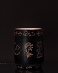 Mate negro grabado con bombilla plateada y fondo negro.