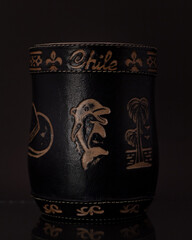 Mate negro grabado con bombilla plateada y fondo negro.