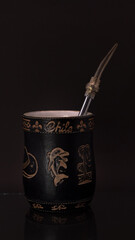 Mate negro grabado con bombilla plateada y fondo negro.