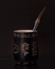 Mate negro grabado con bombilla plateada y fondo negro.