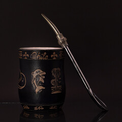 Mate negro grabado con bombilla plateada y fondo negro.