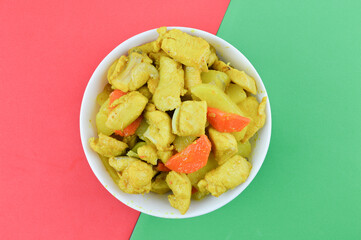 Top view of turmeric chicken in bowl over red and green background