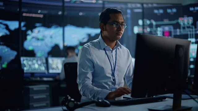 Professional IT Technical Support Specialist and Software Developer Working on Computer in Monitoring Control Room with Digital Screens with Server Data, Blockchain Network and Surveillance Maps. 