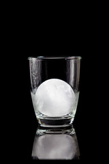 ice ball inside cocktail glass on a reflective black table.