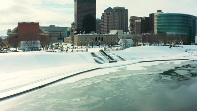 Snowy Drone Shot Of Partially Frozen River With Freshly Fallen Snow Revealing Downtown Dayton Ohio