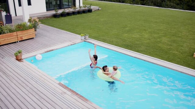 Top view of young family with small daughter in swimming pool outdoors in backyard garden, looking at camera.
