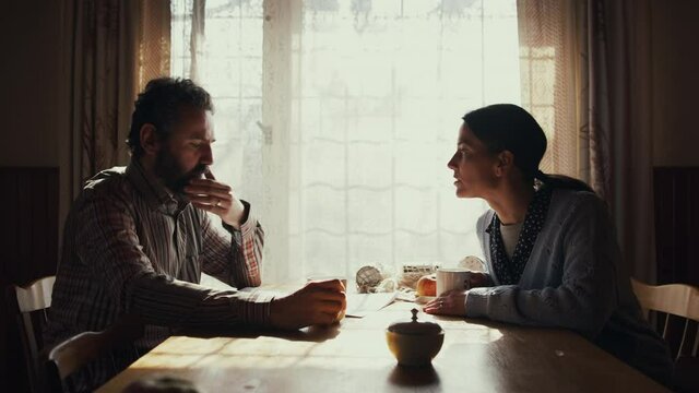 Side view of unhappy poor mature couple reading newspapers indoors at home, poverty concept.
