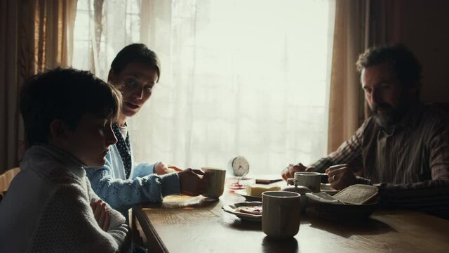 Side view of unhappy poor family having a breakfast indoors at home, poverty concept.