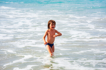 Kid boy playing on the beach on summer holidays. Children in nature with beautiful sea. Happy kids on vacations at seaside running in the water.