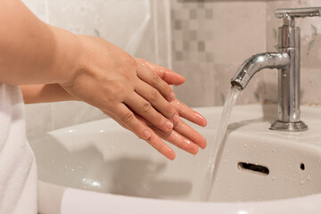 Close-up of young woman washing hands over sink in bathroom at home. hygiene treatment concept