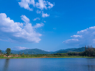 landscape mountain and lake panoramic view with beautiful cirrocumulus clouds popping above lush green mountain in bright clear sunny summer season, blue skycape natural background