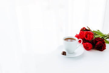 Bouquet of red tulips on table and white coffee cup. Concept for greeting card