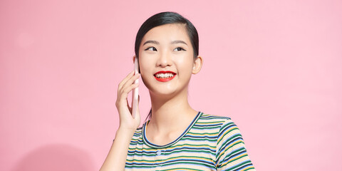 Laughing woman talking on the phone isolated on a pink background