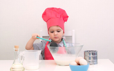 Cute little boy in a red chef hat kneads the pastry dough in a bowl. Homemade cakes