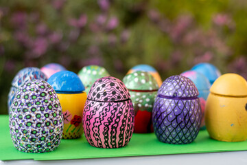 Hand-made Easter eggs on a green pedastal in front of purple lavender flowers.