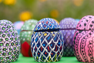 Hand-made Easter eggs on a green pedastal in front of yellow and orange spring flowers