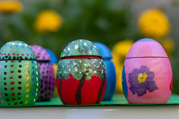 Hand-made Easter eggs on a green pedastal in front of yellow and orange spring flowers