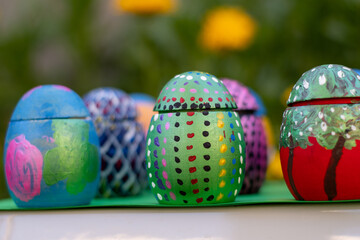 Hand-made Easter eggs on a green pedastal in front of yellow and orange spring flowers