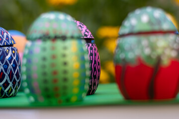 Hand-made Easter eggs on a green pedastal in front of yellow and orange spring flowers