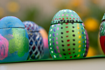 Hand-made Easter eggs on a green pedastal in front of yellow and orange spring flowers