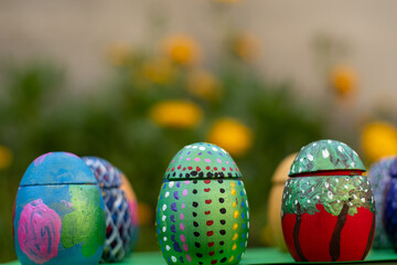 Hand-made Easter eggs on a green pedastal in front of yellow and orange spring flowers