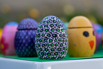 Hand-made Easter eggs on a green pedastal in front of yellow and orange spring flowers