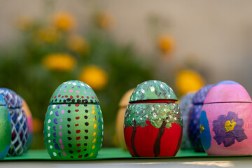 Hand-made Easter eggs on a green pedastal in front of yellow and orange spring flowers