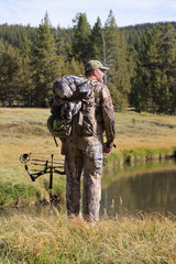 modern bow hunter in woods wearing camouflage and standing by a river