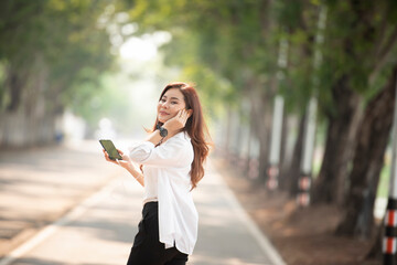 Thai women of Asian descent use a smartphone on the street on a sunny summer day.