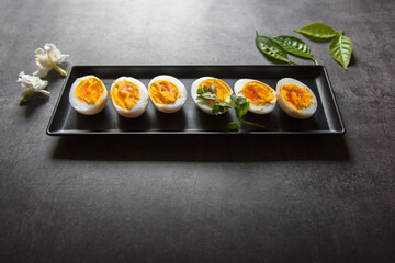 Close up of boiled egg slices in a tray on a dark background.