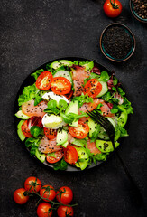Keto diet salad with salted salmon, avocado, egg, sesame seeds, olive oil, tomatoes and mixed herbs. Black background, top view, copy space